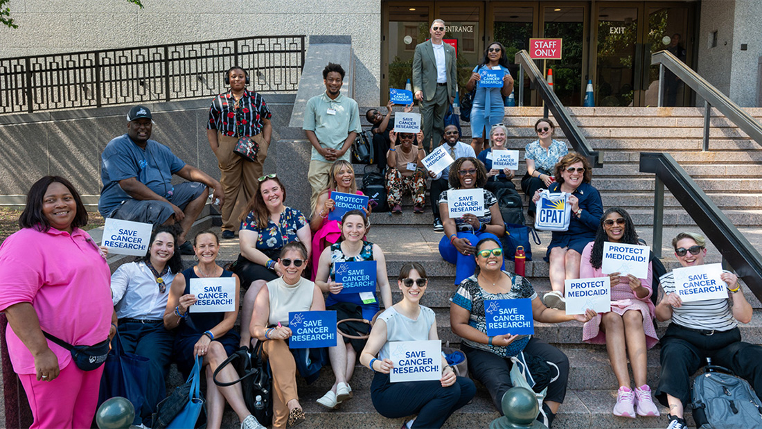 A large group of Cancer Nation Advocates outside a senate office building, many are holding up signs reading Save Medicaid and Save Cancer Research.