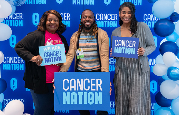 Cancer Nation Advocates posing with Cancer Nation signs at a booth