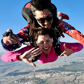 Rebecca Muñoz skydiving with the words "CANCER FREE" written on her hand